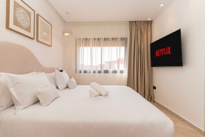 Habitación de hotel con cama, almohadas, televisor en la pared y ventana con cortinas.
