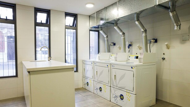 Un cuarto de lavandería con lavamanos, varias lavadoras y conductos de ventilación.