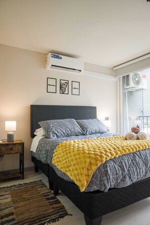 Ein Schlafzimmer mit einem Bett, einem Nachttisch, einer Lampe, einem Fenster mit Blick und einer Klimaanlage.