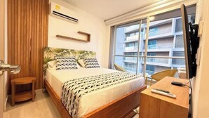Ett hotellrum med en säng, ett skrivbord, en stol, en tv och ett fönster med utsikt över en byggnad.