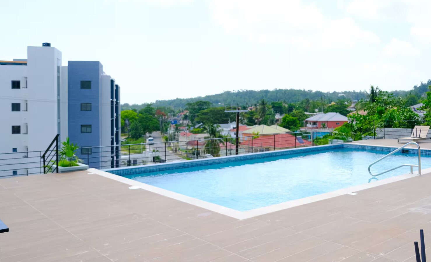 Piscina no terraço com vista para edifícios e vegetação ao redor.
