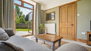 A living room with a sofa, a wooden table, and a potted plant. There is a sliding glass door leading to a garden. - Tranquil countryside cottage (Wrexham)
