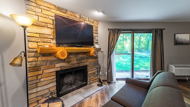 Una sala de estar con chimenea de piedra, un televisor de pantalla plana montado encima y un amplio ventanal con cortinas.