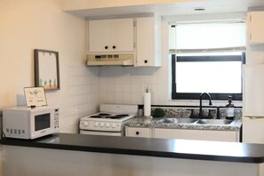 A kitchen with white cabinets, a stove, a microwave, a sink, and a window with blinds. - Marco Island --- Stay in Paradise! (Marco Island)