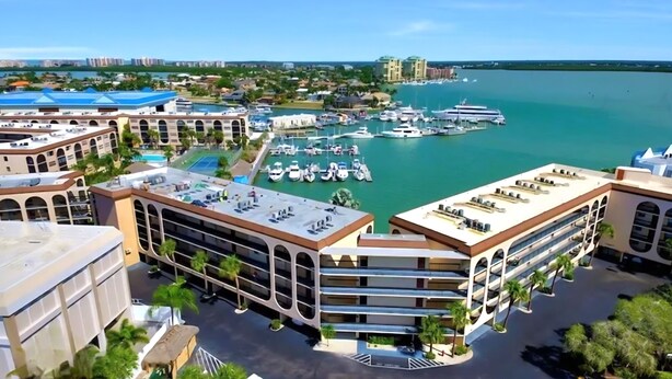 Un port de plaisance avec des bateaux amarrés, un grand bâtiment à étages et une vue dégagée sur l’eau.