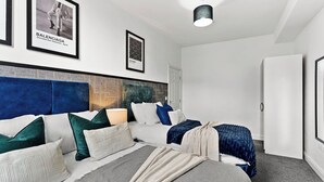 A modern bedroom with a large bed, a headboard with geometric patterns, and framed posters on the wall. - Modern 1BR Flat in Leeds - WiFi (Leeds)