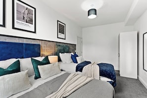 A modern bedroom with a large bed, a headboard with geometric patterns, and framed posters on the wall. - Modern 1BR Flat in Leeds - WiFi (Leeds)