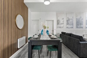 A modern dining area with a dark wooden table, green upholstered chairs, and a grey sofa. - Modern 1BR Flat in Leeds - WiFi (Leeds)