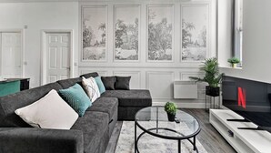 A modern living room with a sectional sofa, a glass coffee table, and a fireplace. - Modern 1BR Flat in Leeds - WiFi (Leeds)