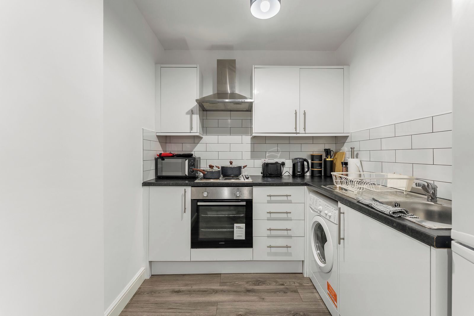 A compact kitchen with a microwave, oven, and washing machine.