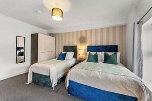 Ein Hotelzimmer mit zwei Betten, einem Schrank, einem Spiegel, einer Wandleuchte und einer gestreiften Wand.