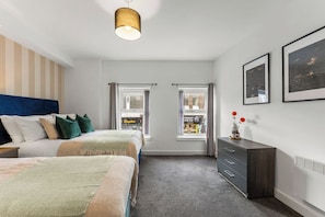Un dormitorio con cama, cómoda, dos ventanas y una lámpara colgante.