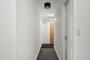 A narrow hallway with white walls, a carpeted floor, and a door at the end. - The Wesley Flat | Elegant Leeds Retreat (Leeds)