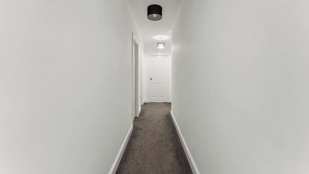 En smal hall med vita väggar, ett mattbeklätt golv och en dörr längst ner.