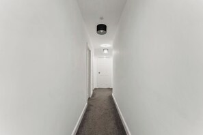 A narrow hallway with white walls, a carpeted floor, and a door at the end. - The Wesley Flat | Elegant Leeds Retreat (Leeds)