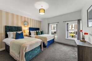 A hotel room with two beds, a large mirror, a hanging light fixture, and a view of the street outside. - The Wesley Flat | Elegant Leeds Retreat (Leeds)