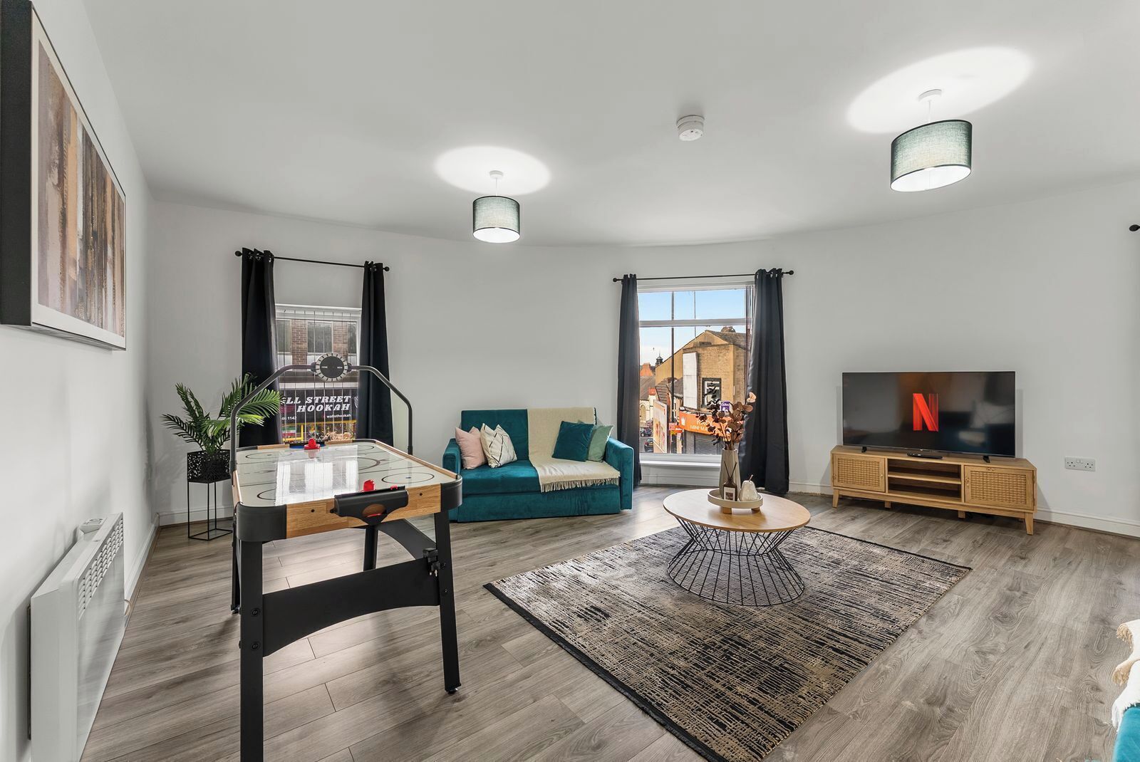 Ein modernes Wohnzimmer mit Billardtisch, einer Couch, einem Fernseher und einem großen Fenster mit Blick auf die Stadt.