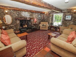 Ein gemütliches Wohnzimmer mit Kamin aus Stein, bequemen Sitzgelegenheiten und Blick ins Freie.