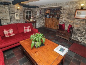 Une pièce chaleureuse avec un canapé rouge, une table basse en bois agrémentée d’une plante, un mur en pierre et un coin bar.