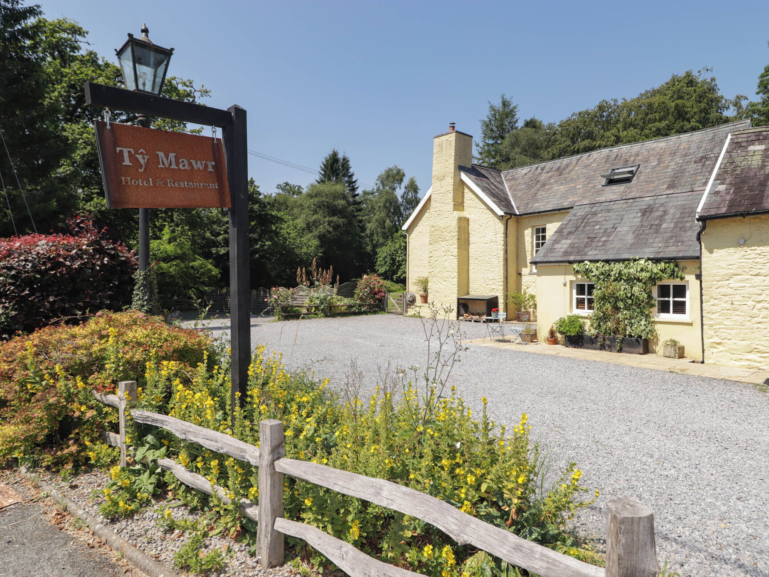 A hotel sign, a stone building with a gravel driveway, and a wooden fence.