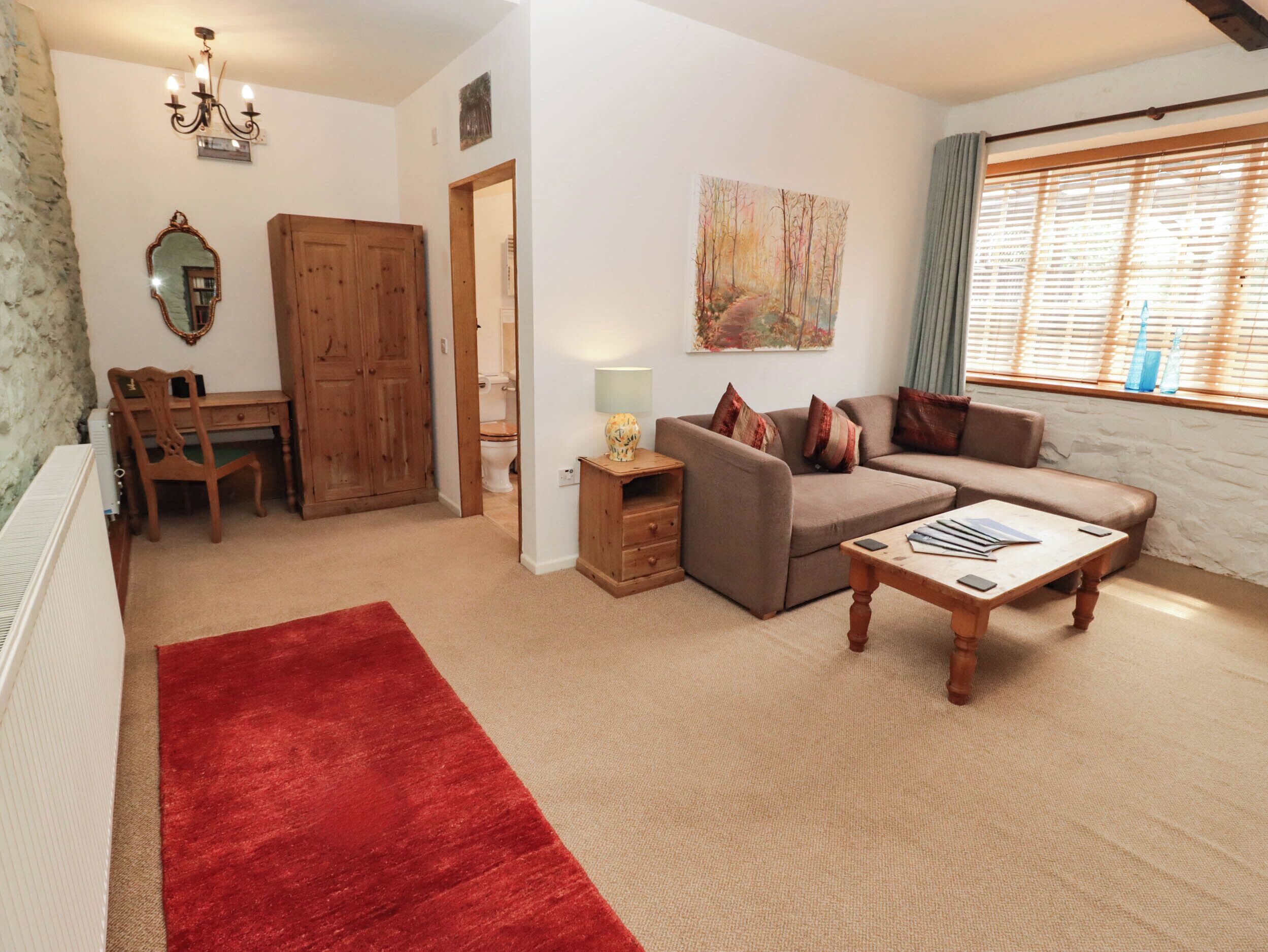 A living room with a sofa, a coffee table, a red rug, a wooden desk, and a door leading to a bathroom.