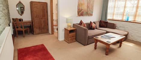 A living room with a sofa, a coffee table, a red rug, a wooden desk, and a door leading to a bathroom.