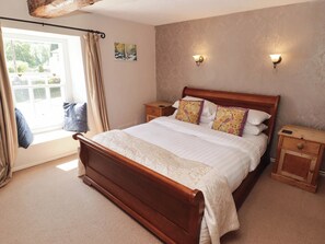 Ein Schlafzimmer mit einem Holzbett, zwei Nachttischen, einem Vorhangfenster und Wandleuchten.