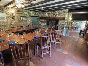 A restaurant with stone walls, wooden tables, and chairs. There is a fireplace and a staircase leading to an upper level. - Ty Mawr Country House (Carmarthen)