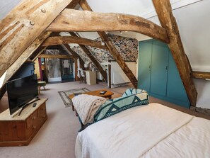 An attic bedroom with a sloped ceiling, wooden beams, a bed, a television on a wooden dresser, and a wardrobe. - Ty Mawr Country House (Carmarthen)