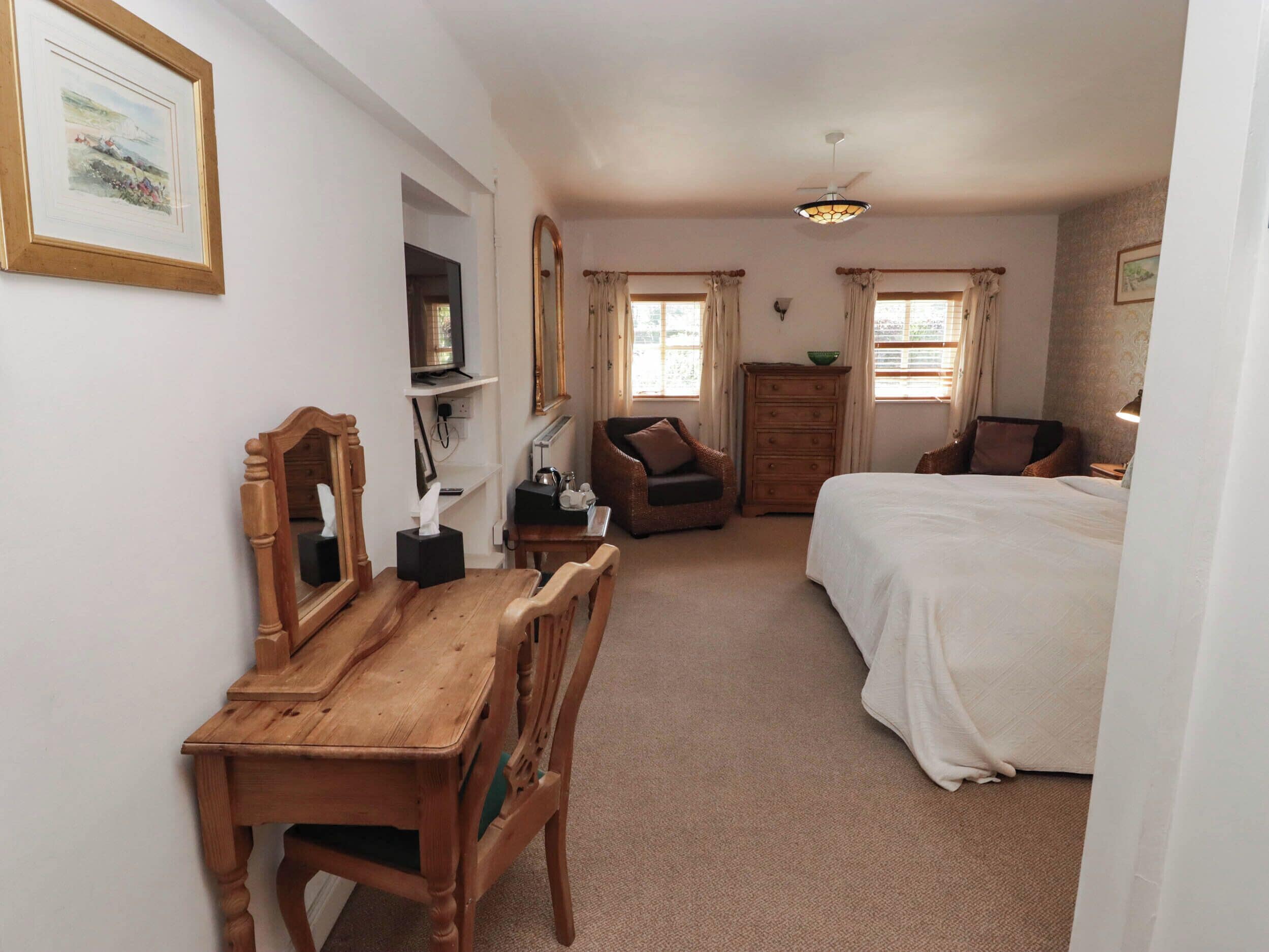A bedroom with a bed, a wooden desk, a chair, a dresser, a mirror, and a television.