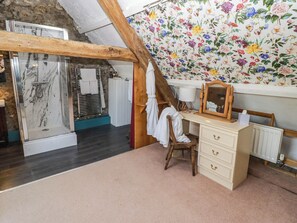 Ein Badezimmer mit Dusche, einem Holzstuhl, einem Schminktisch mit Schubladen und blumengemustertem Wandpapier.