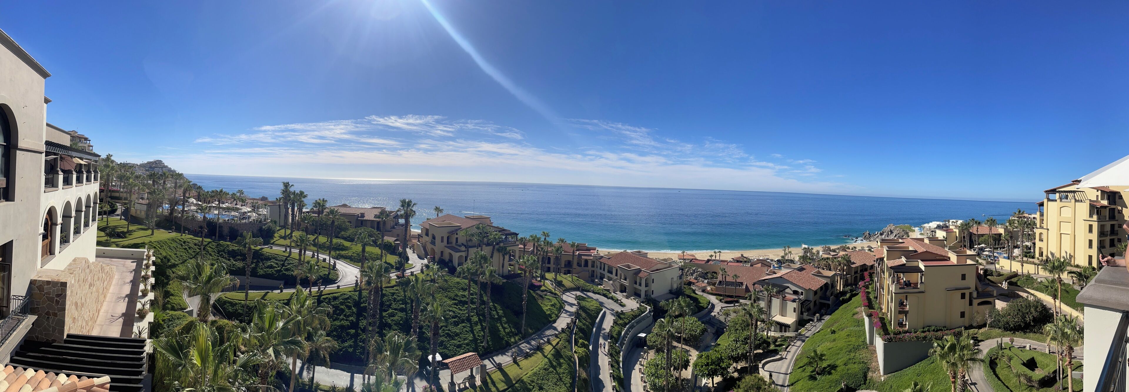 Un resort costero con vistas al océano, que presenta una carretera sinuosa, palmeras y edificios de estilo mediterráneo.