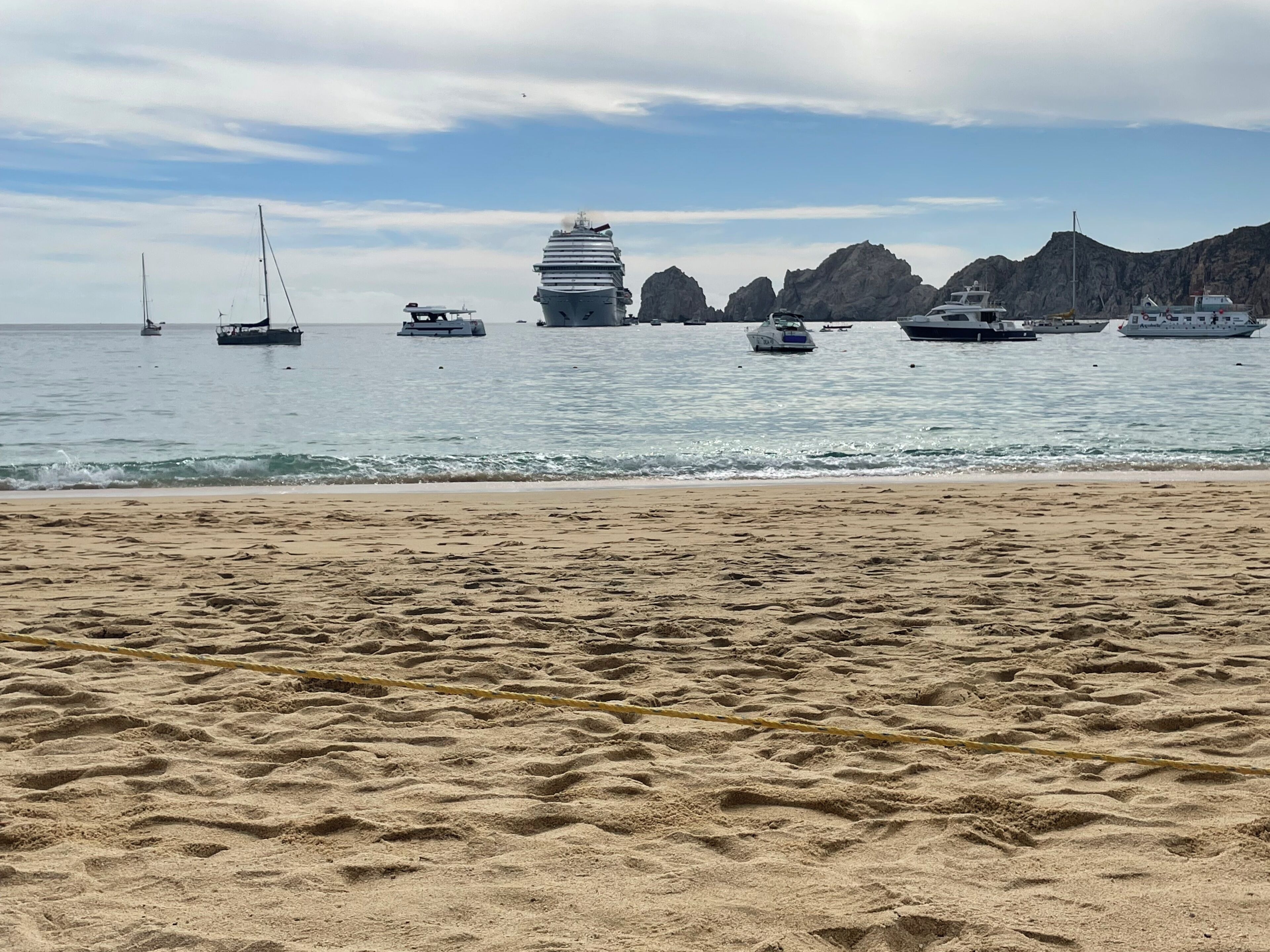 A sandy beach with a large cruise ship docked in the background.