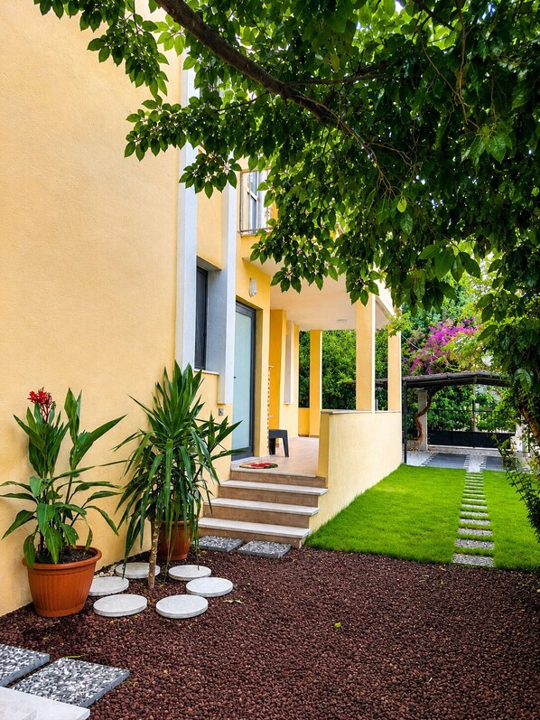 A modern building with a yellow facade, a paved pathway, and potted plants.