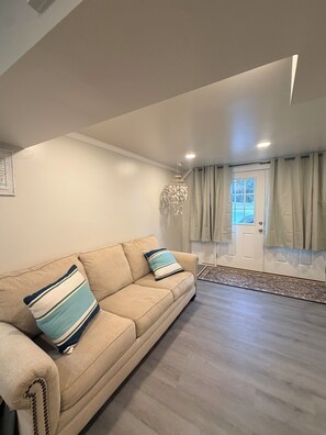 Ein Wohnzimmer mit einem beigefarbenen Sofa, einer Kristallleuchter und einer Tür mit Vorhängen.