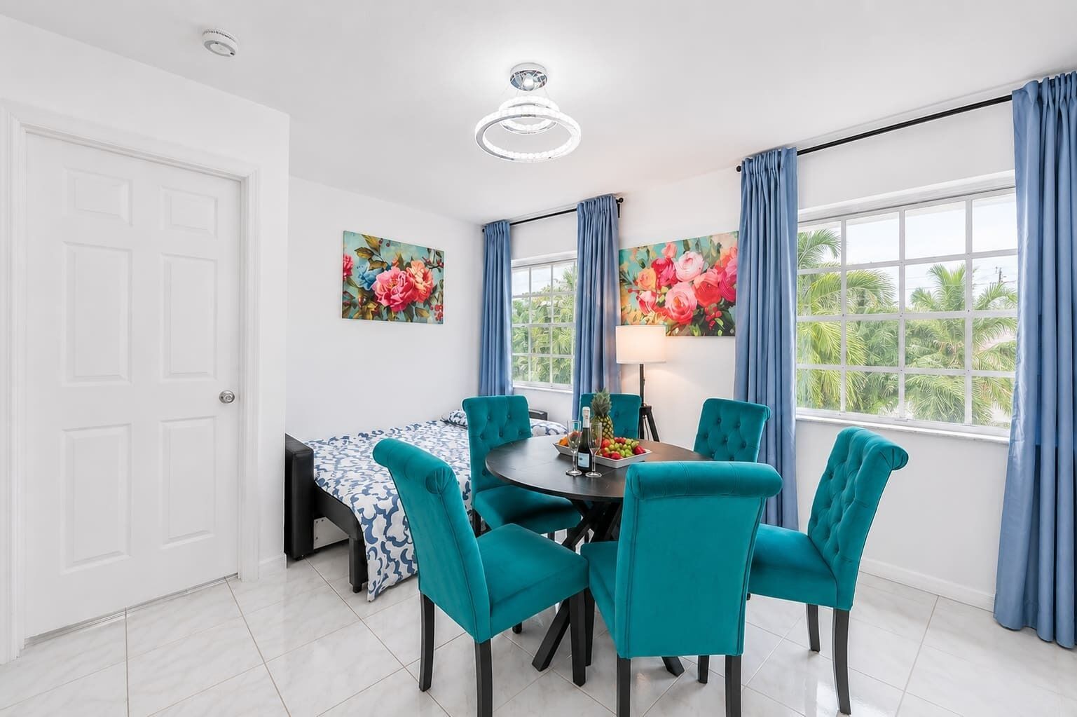 Un comedor con una mesa redonda, sillas color turquesa y un cuadro floral en la pared.