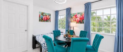 Un comedor con una mesa redonda, sillas color turquesa y un cuadro floral en la pared.