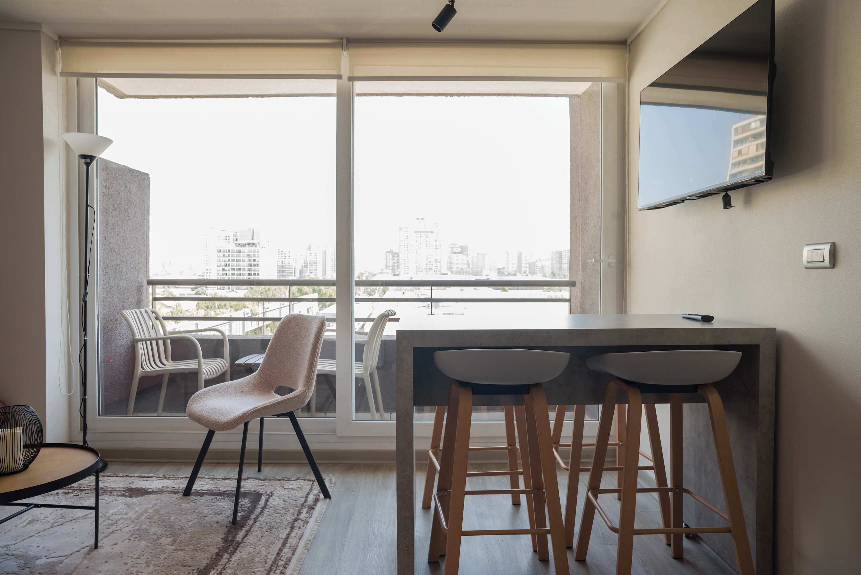 Een modern appartement met een balkon, een eethoek met barstoelen en een flatscreen televisie aan de muur.
