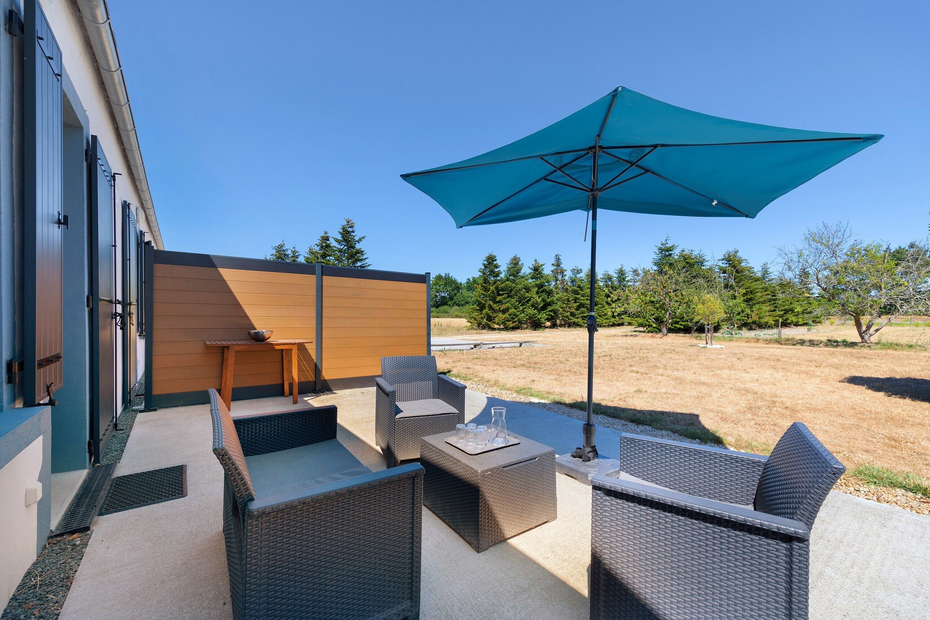 Une terrasse extérieure avec des meubles en osier, une table et un parasol bleu.