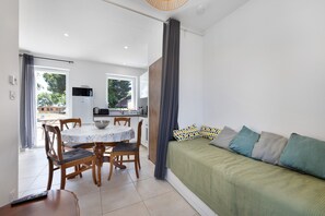 Una sala de estar moderna con un sofá verde, una mesa de comedor con sillas y un área de cocina visible a través de una puerta abierta.