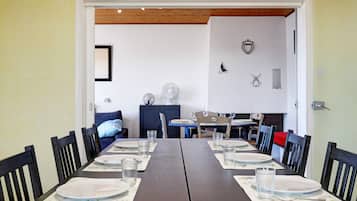 Un coin repas avec une longue table dressée pour deux personnes, des chaises et une vue sur une autre pièce où se trouvent un canapé bleu et un meuble.
