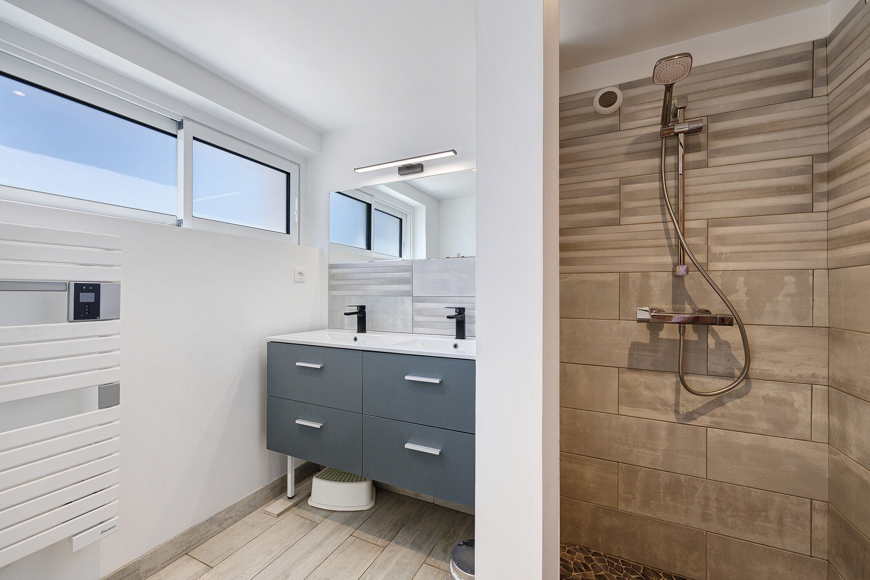 Une salle de bain moderne avec une douche, un meuble-lavabo avec un miroir et une fenêtre.