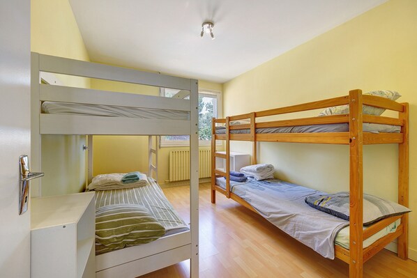 A room with two bunk beds, a white wardrobe, and a window with a view of greenery.