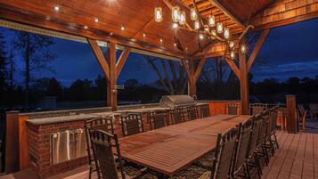An outdoor covered patio with a wooden table and chairs, a grill, and hanging light fixtures.