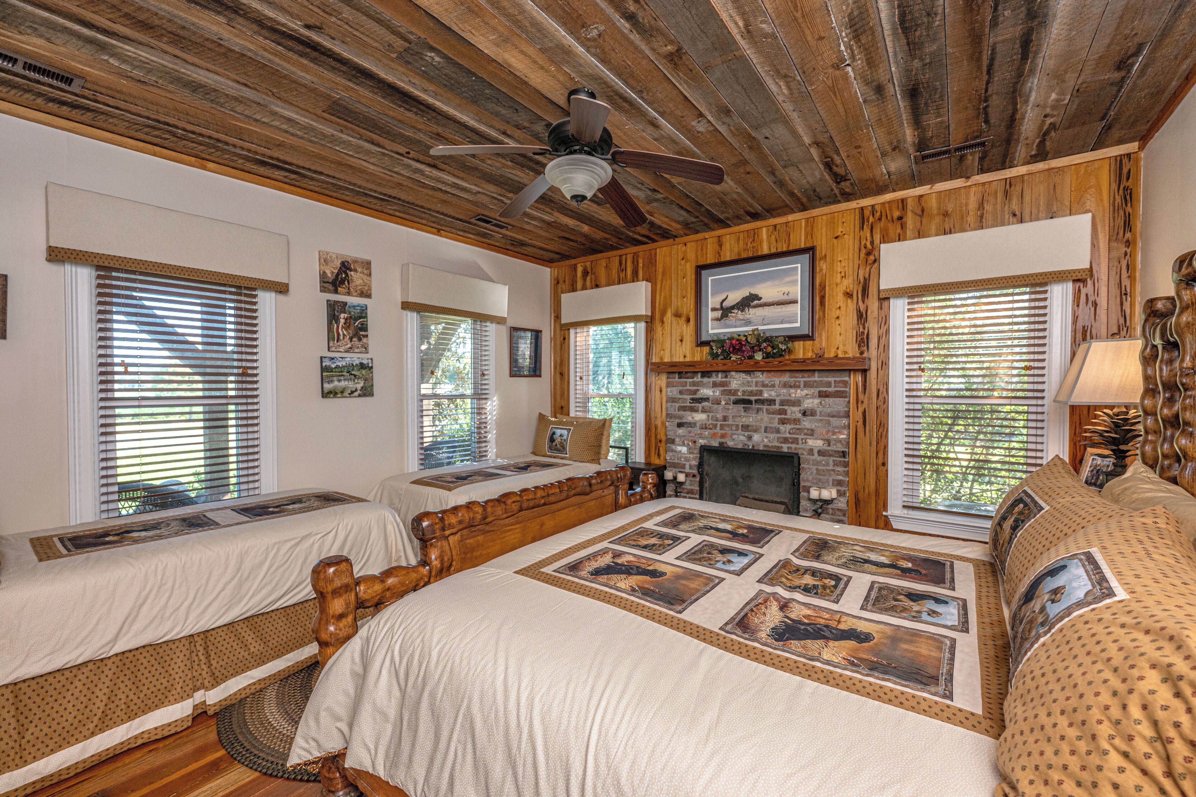 A room with a large bed, two smaller beds, a fireplace, and wooden paneling.