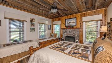 A room with a large bed, two smaller beds, a fireplace, and wooden paneling.