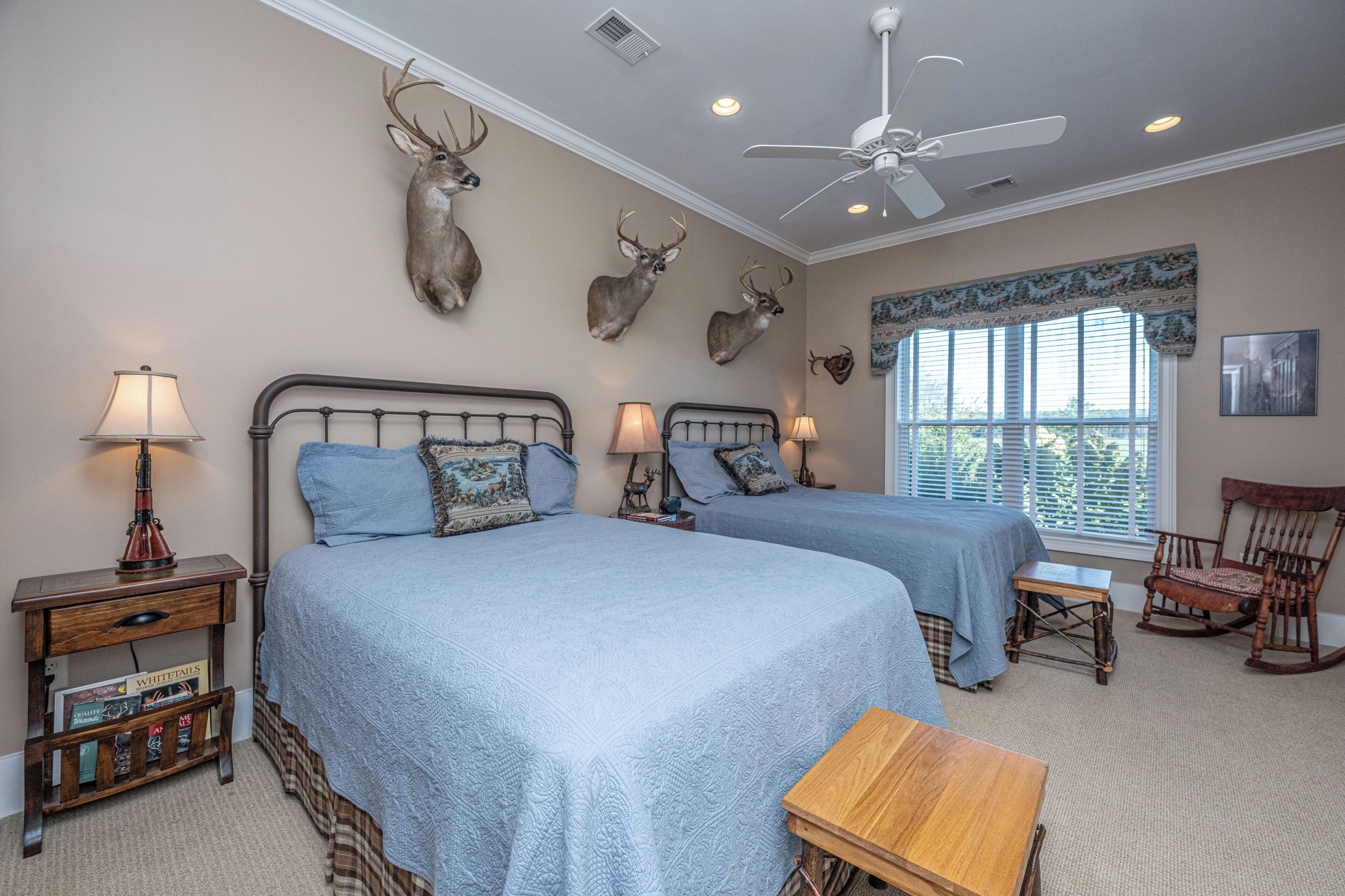 A bedroom with two beds, a ceiling fan, and wall-mounted deer antlers.