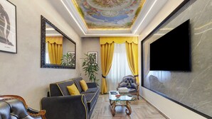 Ein Wohnzimmer mit Sofa, Sesseln, Couchtisch, Fernseher und dekorativer Decke.