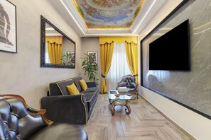 Ein Wohnzimmer mit Sofa, Sesseln, Couchtisch, Fernseher und dekorativer Decke.
