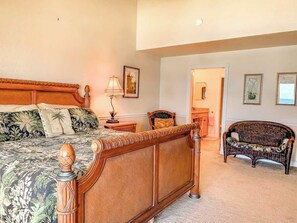 Un dormitorio con cama, mesita de noche, lámpara, silla y puerta que da a otra habitación.